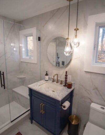 Modern white bathroom with circular mirror and blue furniture - interior designer Litchfield NH