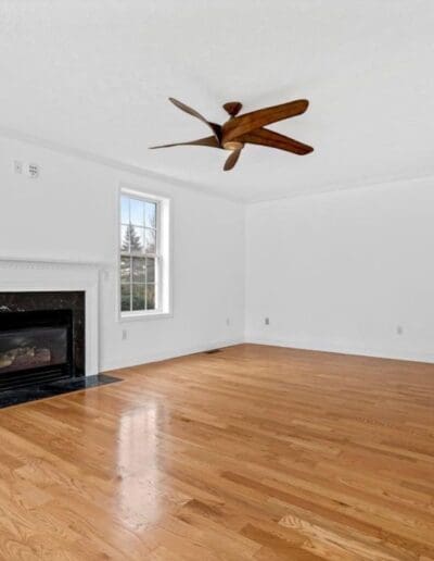 Empty living room with fireplace, two windows and ceiling fan - interior designer Bedford NH